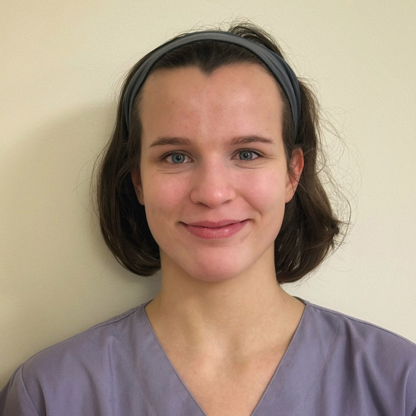 Junge Frau mit braunen Haaren und Stirnband lächelt freundlich in grauer Kleidung