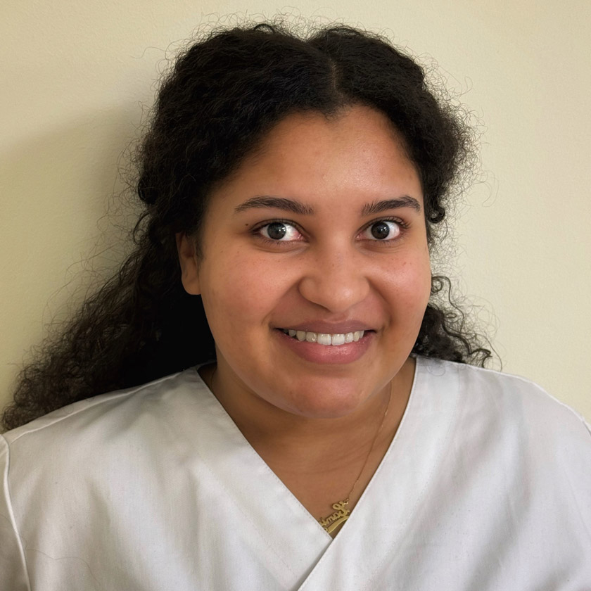 Junge Frau mit lockigem dunklem Haar lächelt freundlich in weißer Kleidung